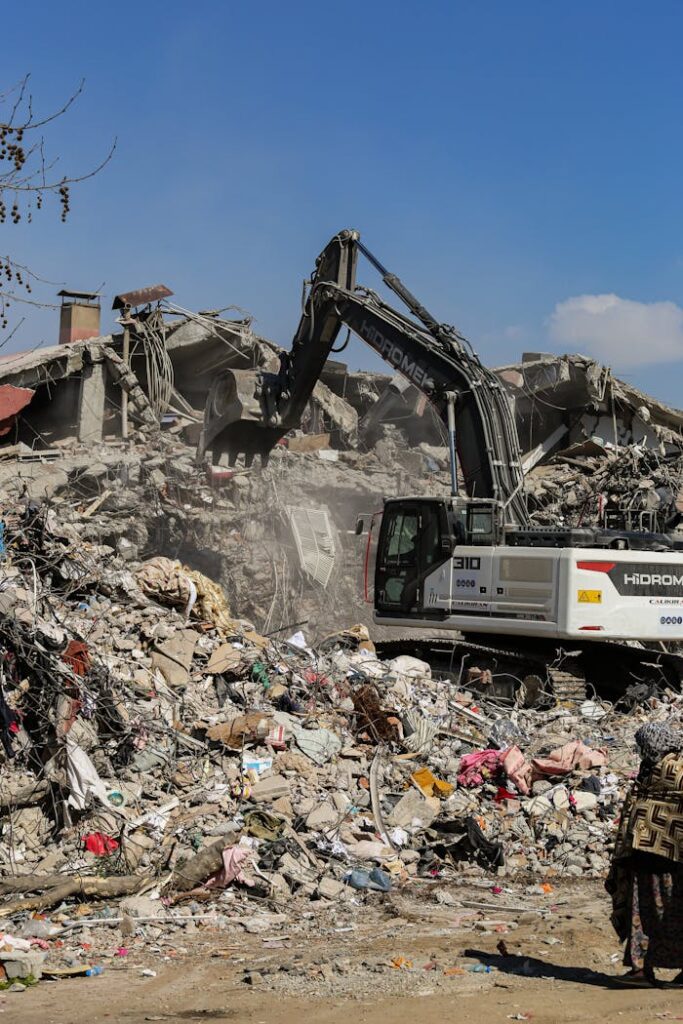 Excavator working among rubble in ruins on a clear day, symbolizing reconstruction.