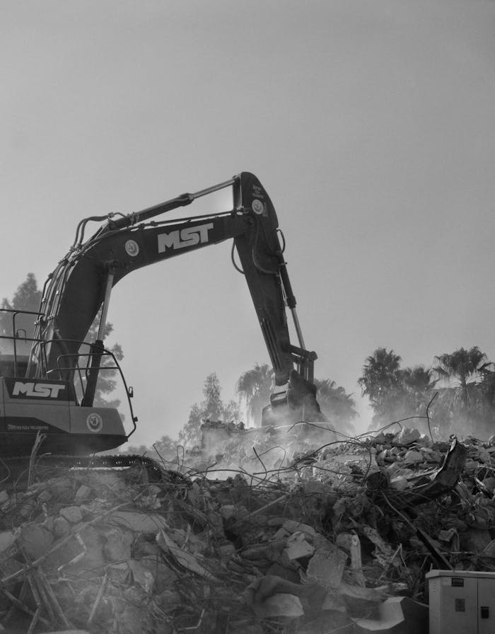 A powerful excavator working amidst rubble and dust at a construction site.